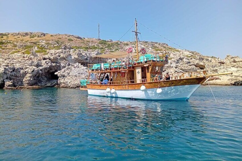 A wooden boat with blue accents docked near rocky cliffs. 1