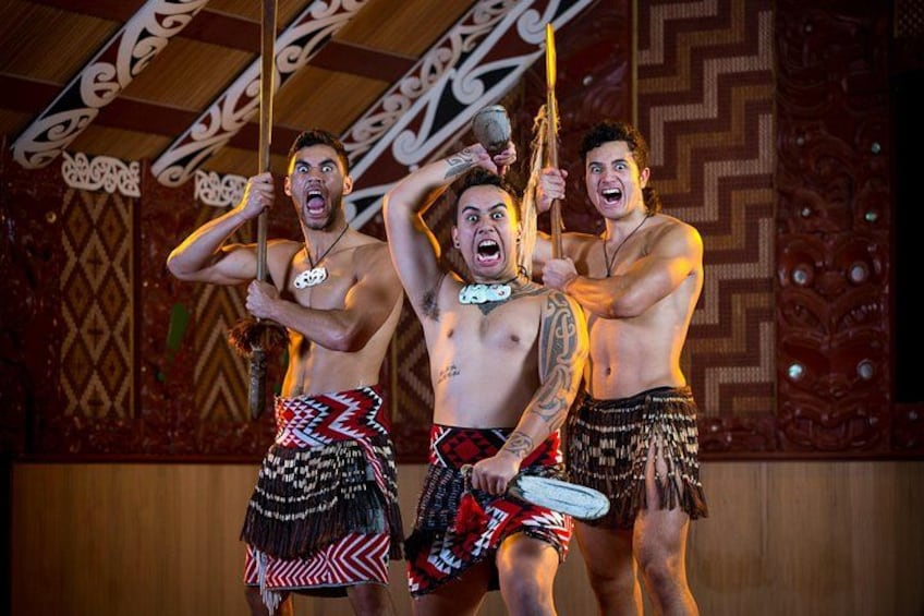 Three individuals in traditional attire holding objects, standing in a room with patterned walls. 2