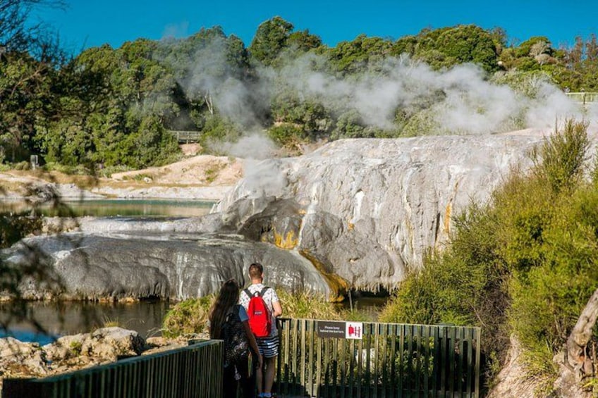 A geothermal area with steam vents, a person standing by a fence, and a signboard. 4