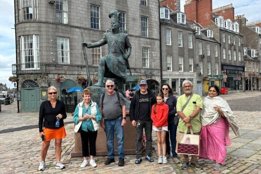 A group of people standing in front of a statue on a cobblestone street with historic buildings in the background. 5