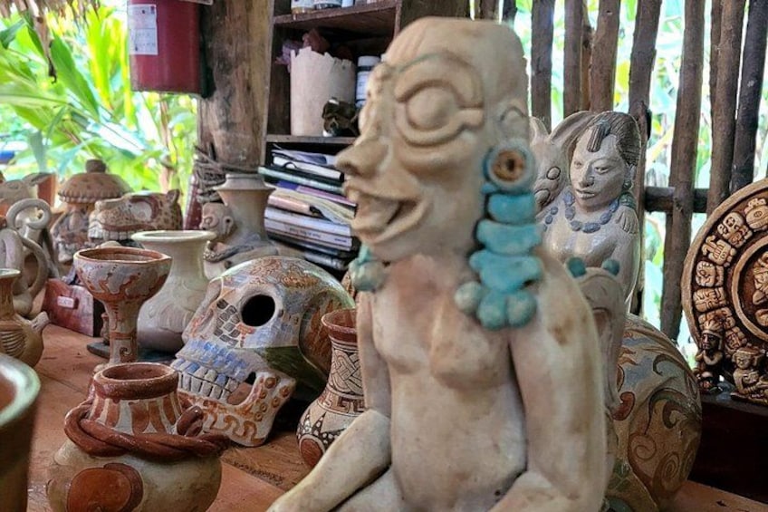 A collection of pottery and sculptures, including a prominent figure with a blue necklace. 1