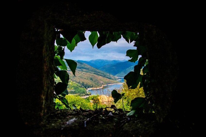 A view through a window with greenery framing a landscape of hills and a river. 4