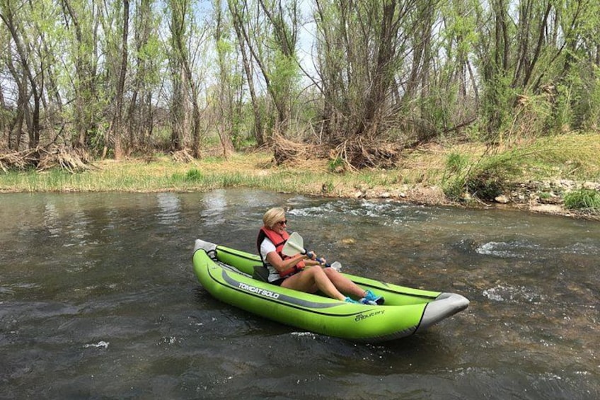 A person in a green kayak on a river surrounded by trees. 1