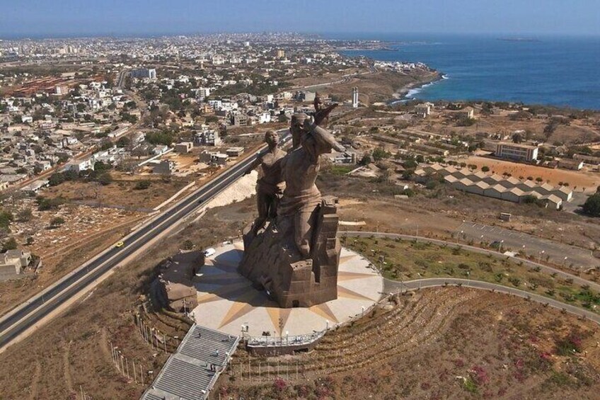 A statue of a man on a pedestal surrounded by a circular plaza, with a coastal cityscape in the background. 5
