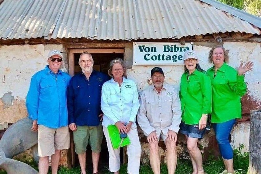 A group of people standing in front of a rustic building with a sign that reads 'Von Bibra Cottage.' 2