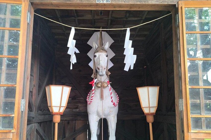 A white horse statue in a wooden stable with two lanterns and paper decorations. 5
