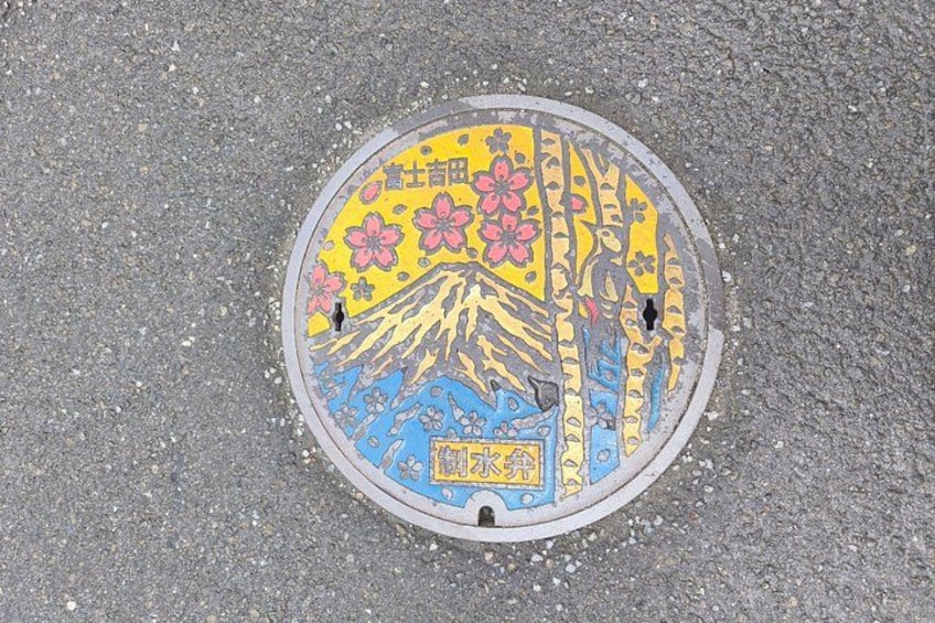 A manhole cover with a colorful design featuring cherry blossoms and a mountain. 4