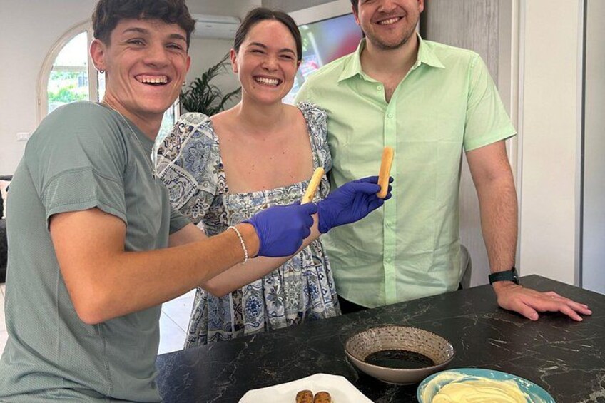 Three people in a kitchen, one holding a baguette. 1