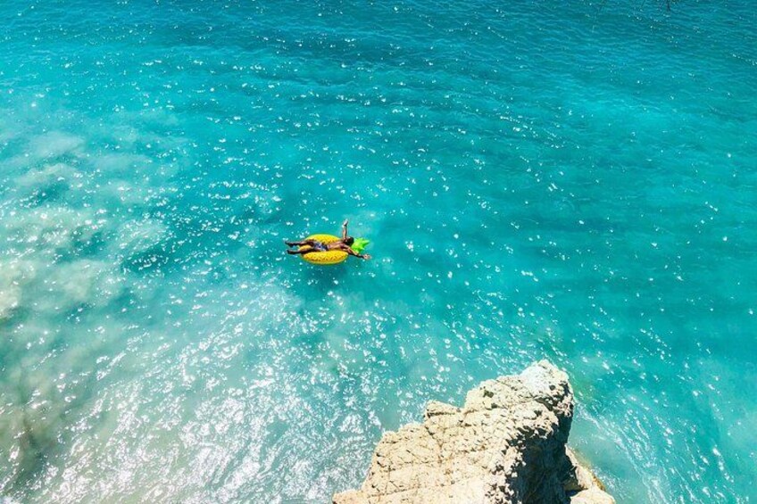 A person floating on a yellow raft in turquoise water with a rocky shoreline. 1