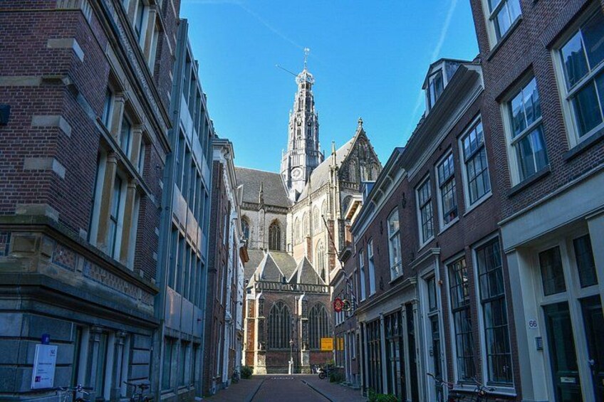 A street leading to a church with a tall spire, surrounded by brick buildings with large windows. 2