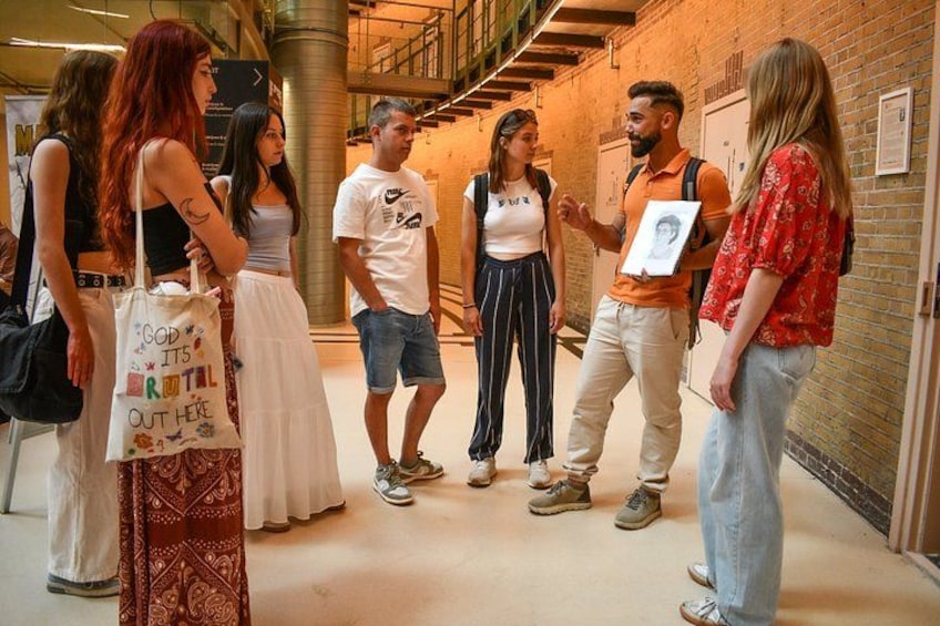 A group of people standing in a corridor with brick walls and a staircase in the background. 5