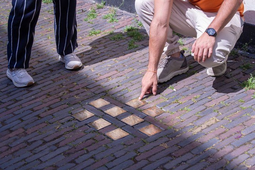 A person pointing at a brick pavement with a square pattern. 4