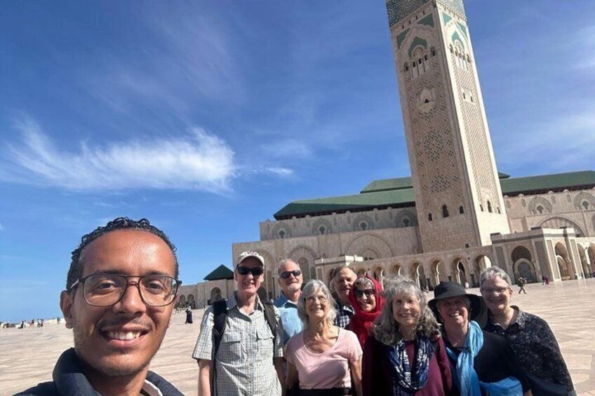 Een groep mensen staat voor een groot, historisch gebouw met een hoge toren en bogen. 1