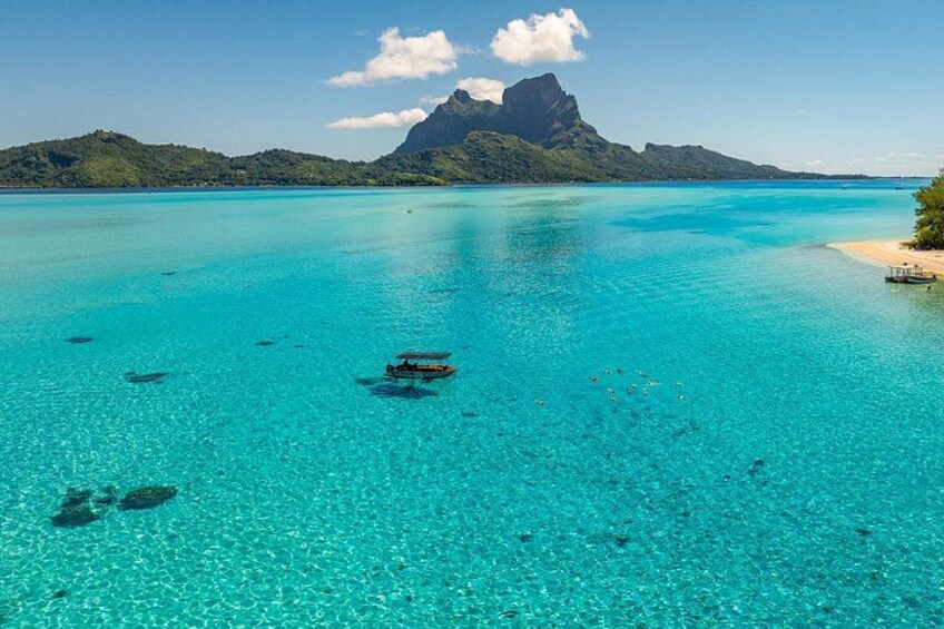 A turquoise sea with boats, a sandy beach, and a mountain in the background. 1