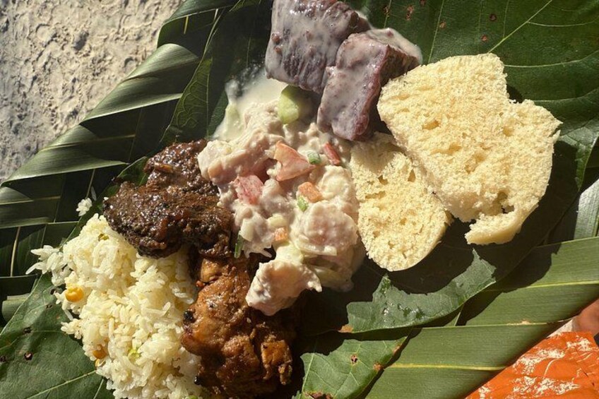 A meal served on a banana leaf with rice, meat, a purple dessert, and bread. 4