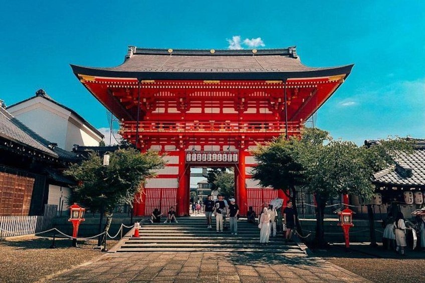 Un tradicional torii japonés con estructura roja y techo negro, que da paso a un sendero con gente caminando. 3