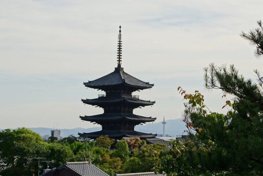 Een traditionele Japanse pagode met meerdere verdiepingen, omgeven door weelderig groen en een verre uitzicht op een toren. 4