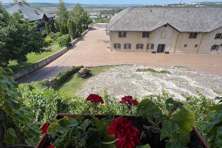 A building with a stone facade, a paved courtyard, and a view of a body of water in the distance. 3