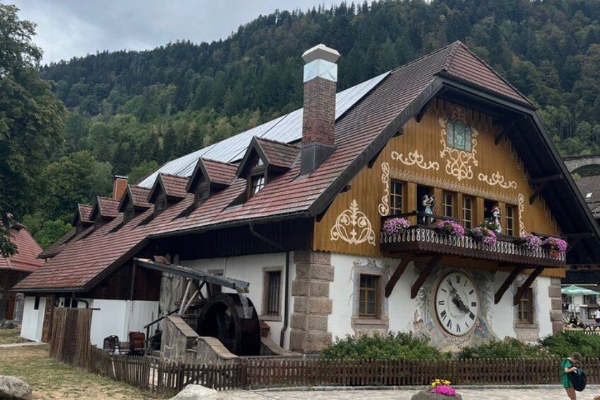 A traditional wooden house with a sloped roof, a large water wheel, and a clock. 2