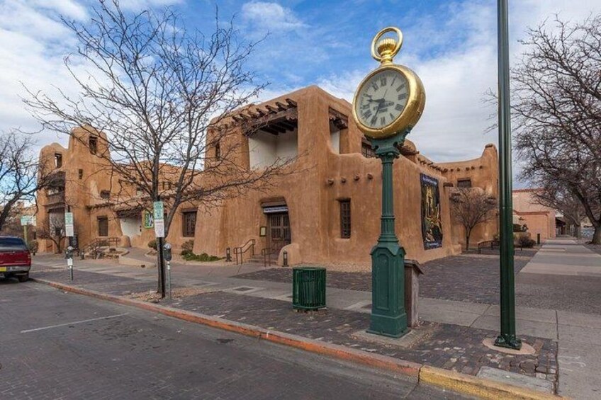 Un edificio histórico de adobe con un reloj de calle y un cielo azul despejado. 5