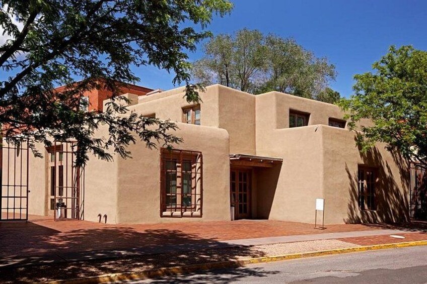 Un edificio con techo plano y paredes de estuco, una puerta roja y un ventanal pequeño. 3