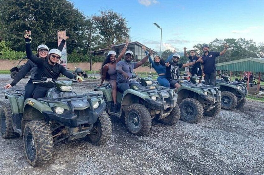 A group of people on ATVs in a gravel area with trees and a building in the background. 2