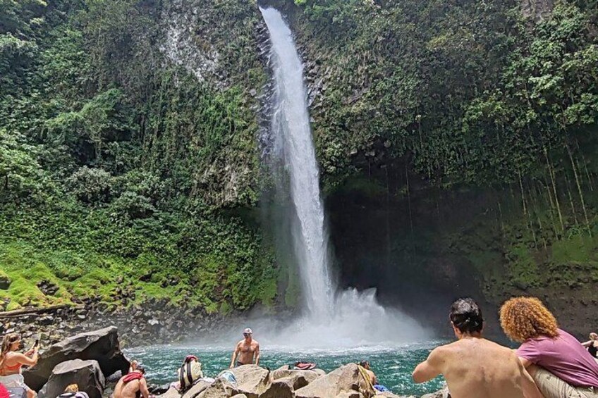 A waterfall, lush greenery, and people enjoying the natural setting. 1