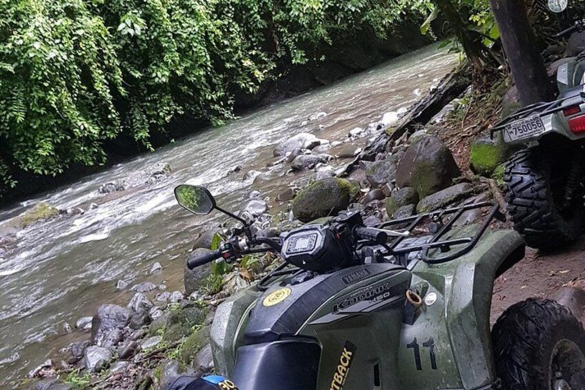 A green ATV parked by a rocky riverbank with a flowing river in the background. 4