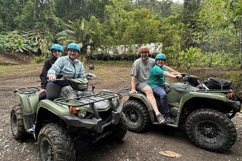 Two people on green all-terrain vehicles in a natural setting with trees and a dirt path. 3