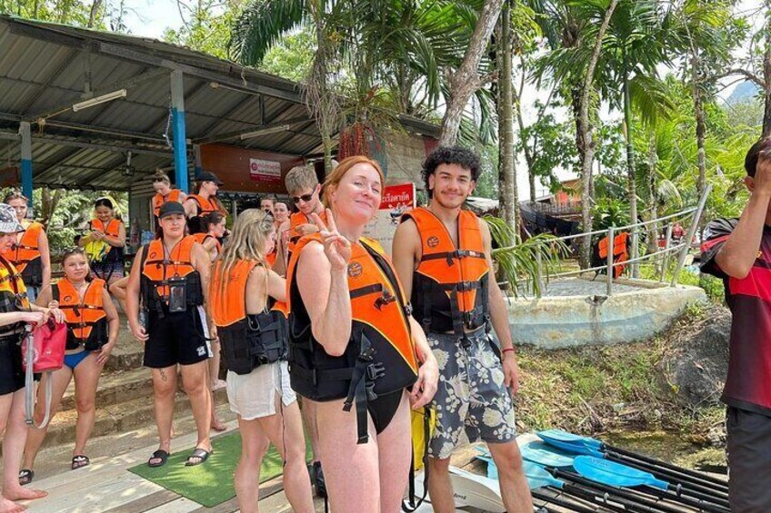 People in orange life vests standing near a pool with paddleboards. 2