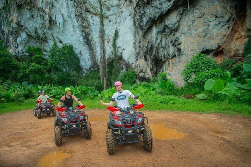 Three people riding ATVs on a dirt path with a rocky cliff in the background. 4