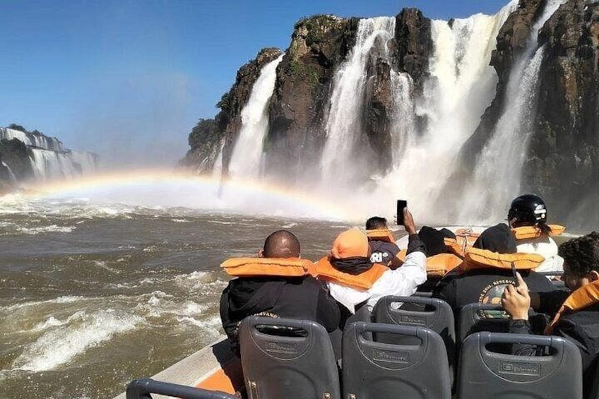 Un grupo de personas en un bote observando una cascada con un arcoíris. 3
