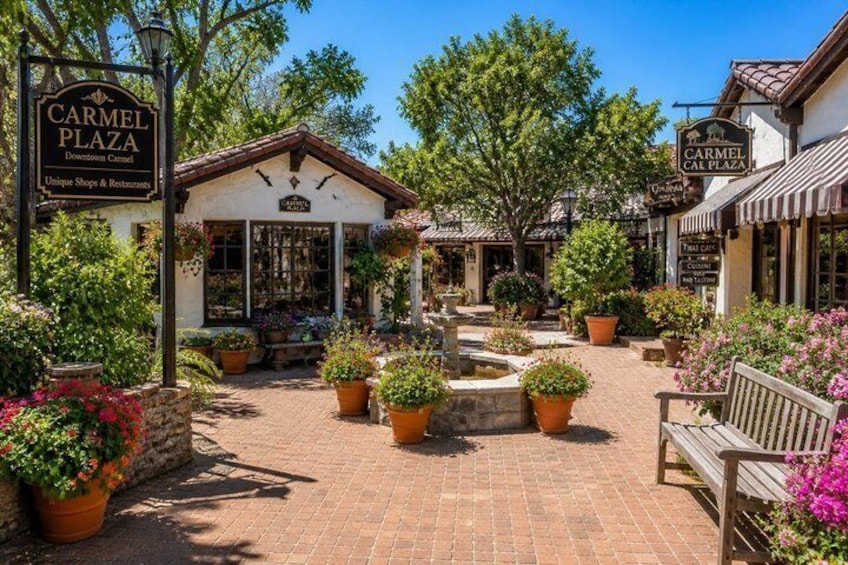A brick plaza with potted plants and a bench, surrounded by buildings with 'CARMEL PLAZA' signs. 2