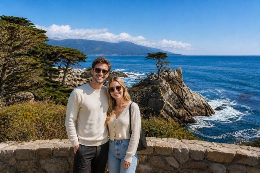 A couple standing on a stone wall overlooking a coastal landscape with a prominent rocky outcrop and a lone tree. 4