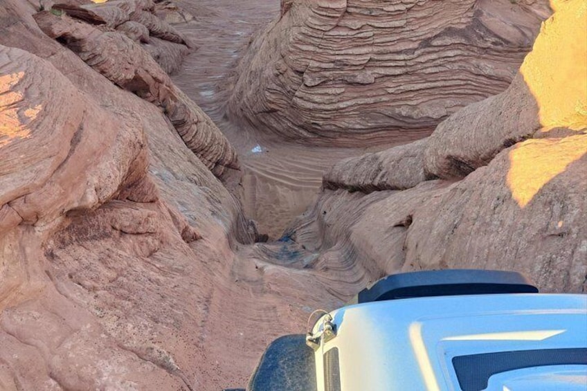 Eine zerklüftete Schlucht mit schichtartigen Gesteinsformationen und einem teilweise sichtbaren Fahrzeug am Grund. 3