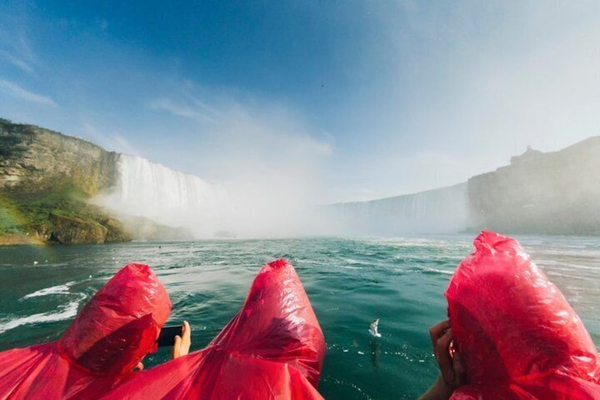 A boat with people in red rain ponchos facing a waterfall. 2