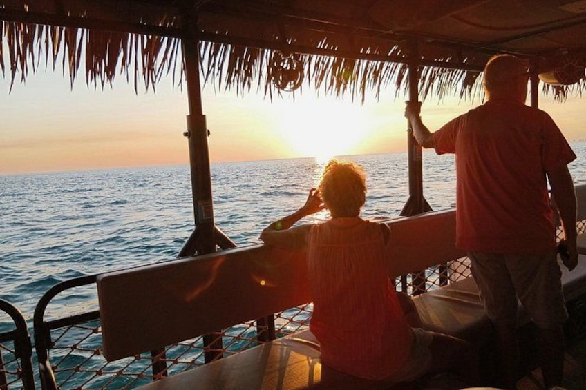 Een boot met een rieten dak, twee personen en een zonsondergang boven de oceaan. 3