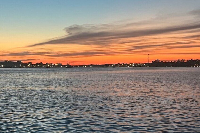 A sunset over a body of water with city lights in the distance. 3