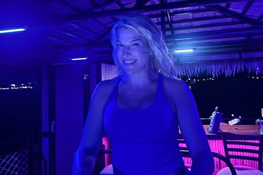 A person in a blue top standing in a room with a thatched roof and a bar area in the background. 2