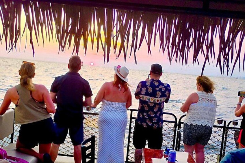 Een groep mensen op een boot, een zonsondergang en een rieten dak. 4