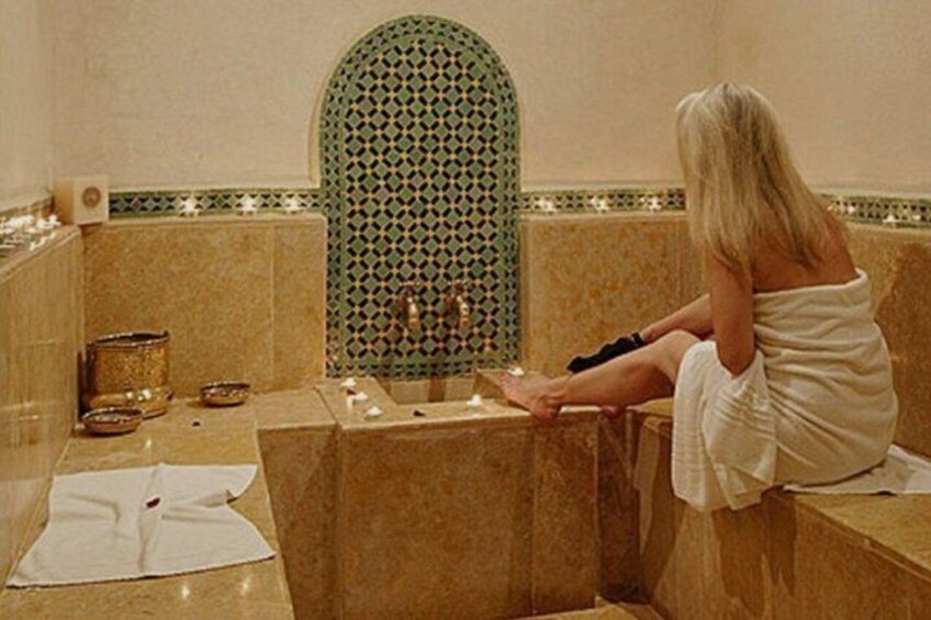 A person sitting on a bench in a bathroom with a tiled wall and a sink. 3