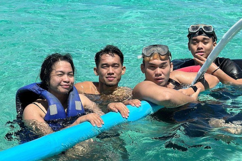 Four people in clear water, wearing life jackets, with one person holding a blue floatation device. 1