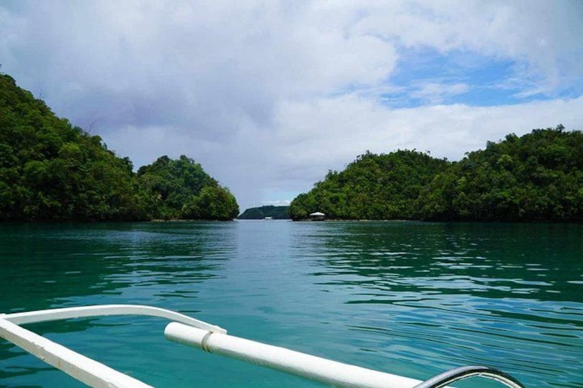 A boat on calm turquoise water with dense green forested islands in the distance. 3