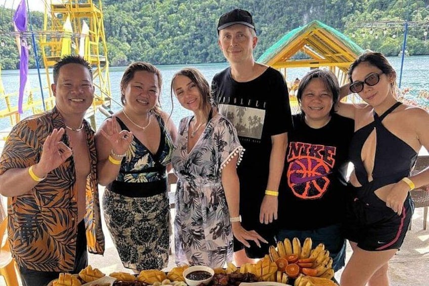 A group of people posing by a table with food and a yellow structure in a tropical setting. 2