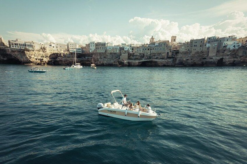 Un bateau avec des personnes à bord, naviguant sur une mer calme, avec une côte rocheuse et des bâtiments en arrière-plan. 1
