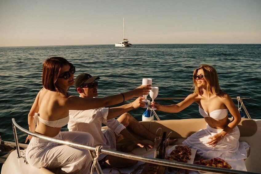 Un groupe de personnes se trouve sur un bateau, tenant des verres à vin, et un voilier est visible à l’arrière-plan. 5