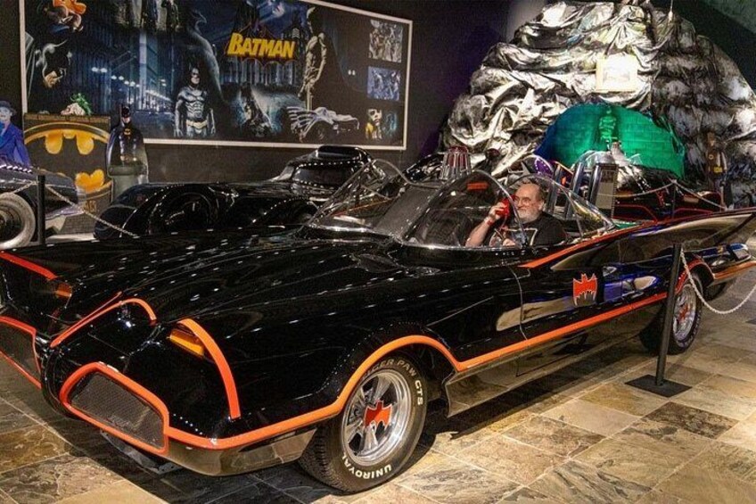 Une voiture décapotable noire avec des touches de couleur orange, exposée dans un musée sur fond décoré aux couleurs de Batman. 3