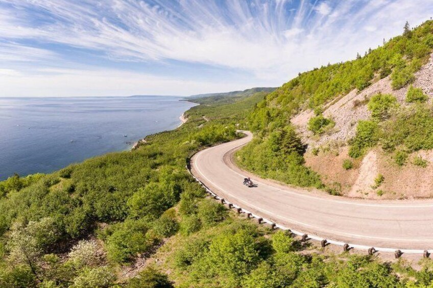 A winding coastal road with a motorcyclist, surrounded by lush greenery and overlooking the sea. 5