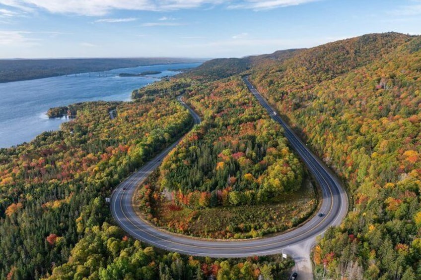 A winding road through a forested area with a body of water in the background. 1