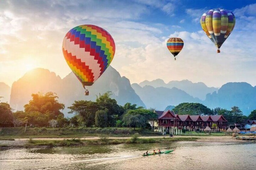 A river with hot air balloons, a traditional building, and mountains in the background. 2